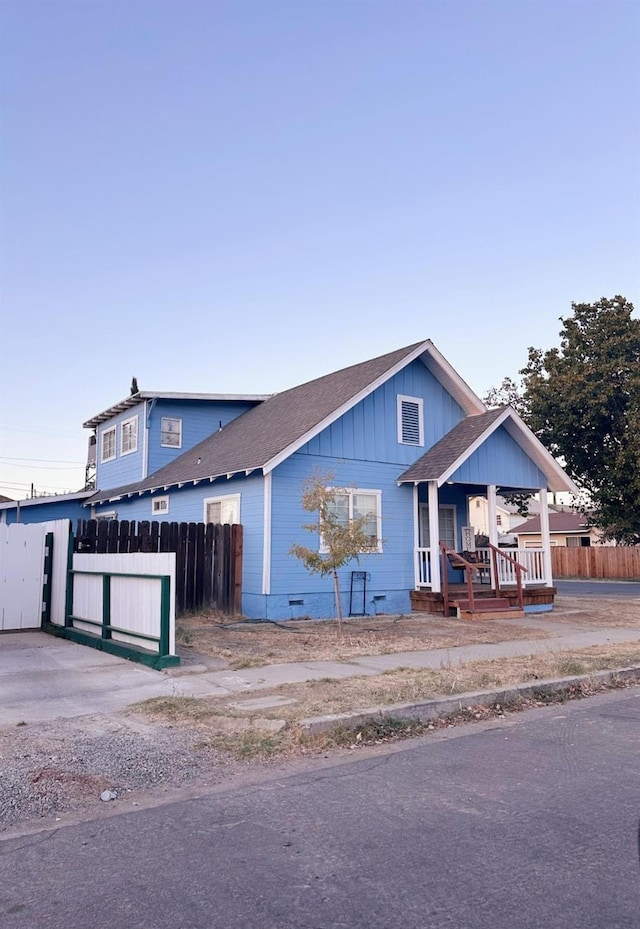 view of front of property featuring a shingled roof, covered porch, board and batten siding, crawl space, and fence