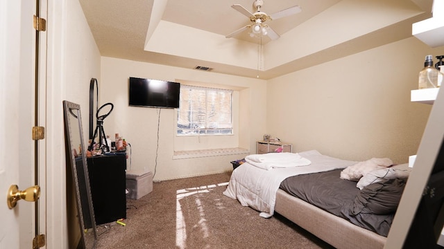 carpeted bedroom featuring a ceiling fan, a raised ceiling, and visible vents