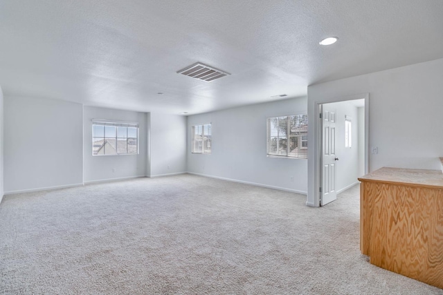 unfurnished room with light carpet, baseboards, visible vents, and a textured ceiling