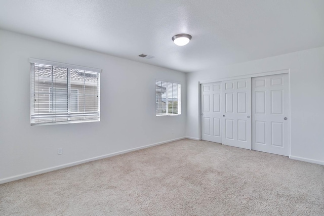 unfurnished bedroom featuring light carpet, a closet, visible vents, and baseboards