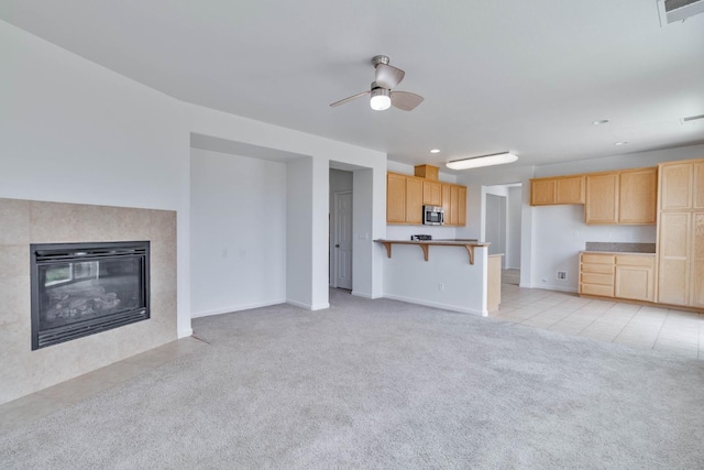 unfurnished living room with ceiling fan, light tile patterned floors, a tile fireplace, light colored carpet, and visible vents