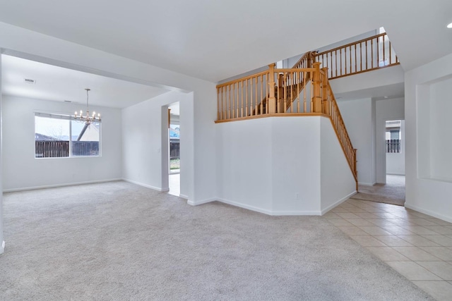 spare room featuring a chandelier, light tile patterned floors, light colored carpet, baseboards, and stairway