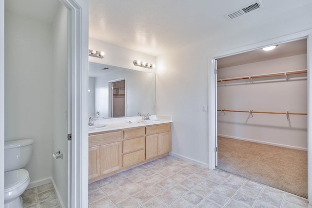 bathroom with toilet, double vanity, a sink, and visible vents