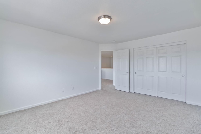 unfurnished bedroom with light carpet, baseboards, and a closet