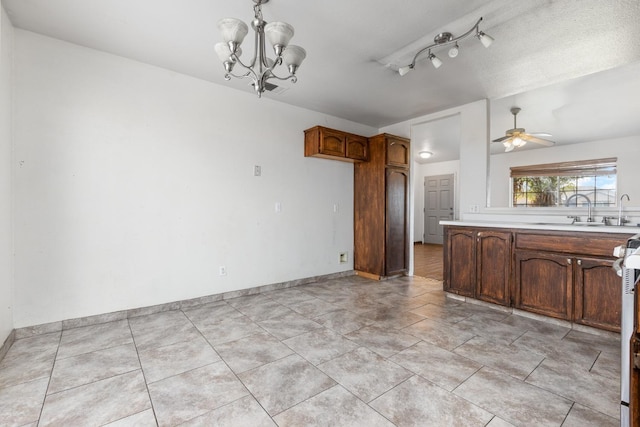 kitchen featuring ceiling fan with notable chandelier, light countertops, a sink, and baseboards