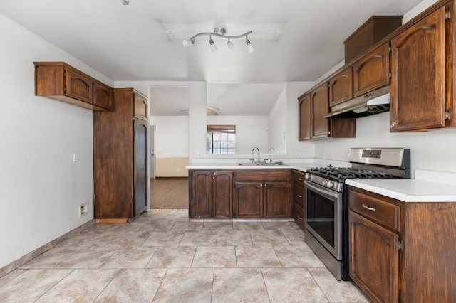 kitchen with light tile patterned floors, under cabinet range hood, a sink, light countertops, and stainless steel range with gas stovetop