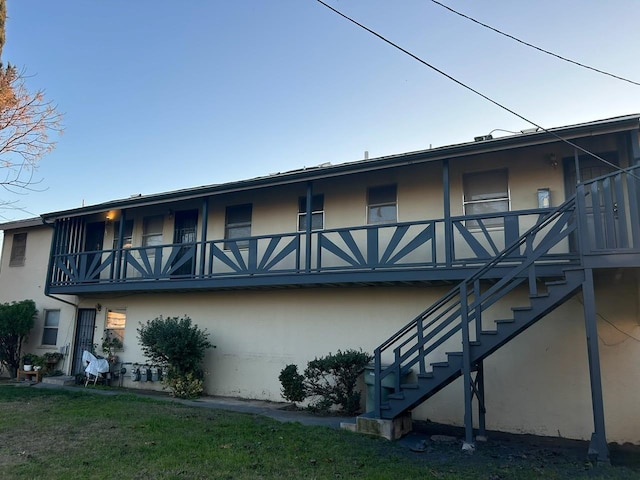 back of house with stairs, a yard, and stucco siding