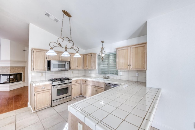 kitchen with tile countertops, appliances with stainless steel finishes, backsplash, light brown cabinetry, and pendant lighting