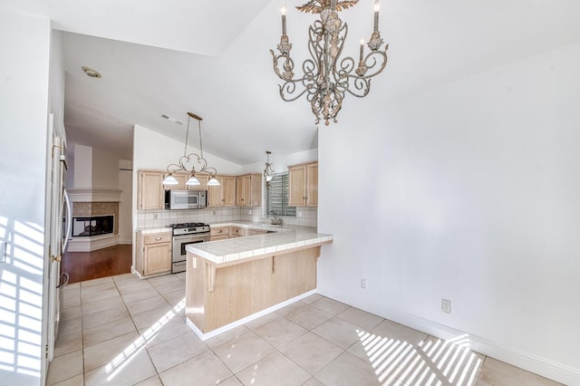 kitchen with appliances with stainless steel finishes, a peninsula, light brown cabinets, a chandelier, and a sink