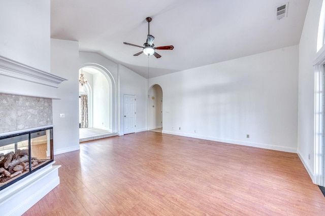 unfurnished living room featuring arched walkways, a tiled fireplace, wood finished floors, vaulted ceiling, and ceiling fan with notable chandelier