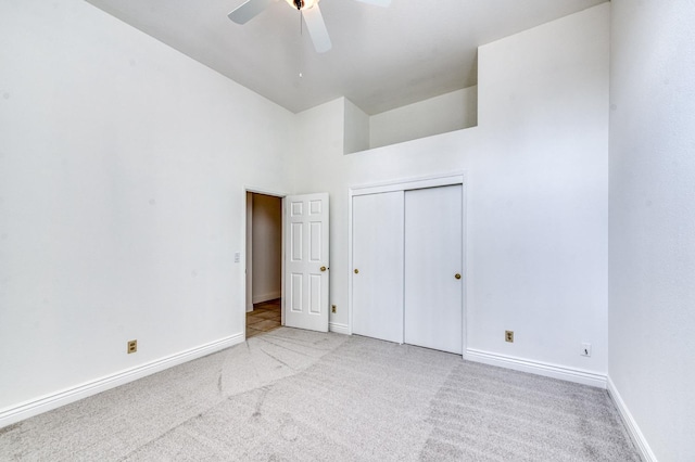 unfurnished bedroom with light carpet, baseboards, a ceiling fan, a high ceiling, and a closet