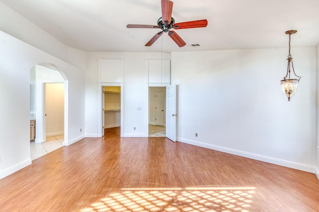 interior space featuring baseboards, visible vents, arched walkways, ceiling fan, and light wood-style floors