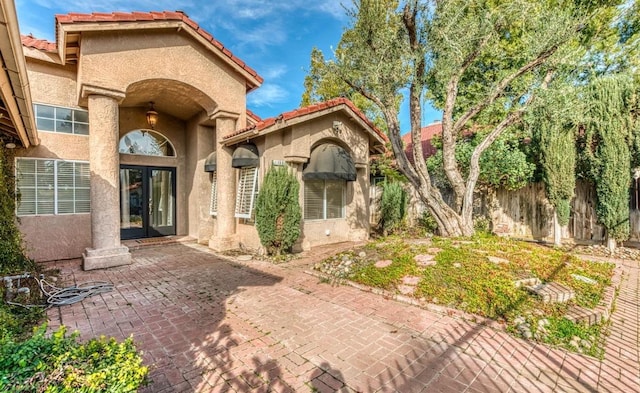 property entrance featuring fence, a tiled roof, french doors, stucco siding, and a patio area