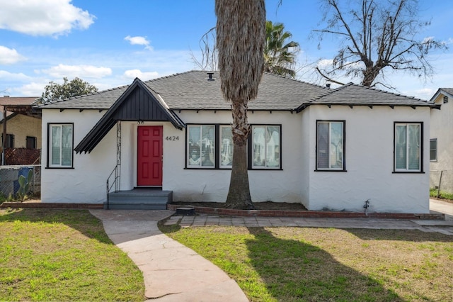 view of front facade featuring entry steps, roof with shingles, a front yard, board and batten siding, and stucco siding