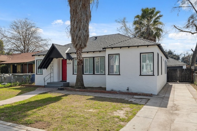 bungalow-style house with a front lawn, roof with shingles, fence, and stucco siding