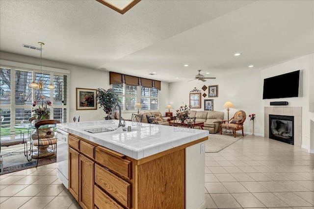 kitchen with tile countertops, light tile patterned floors, white dishwasher, a fireplace, and a sink