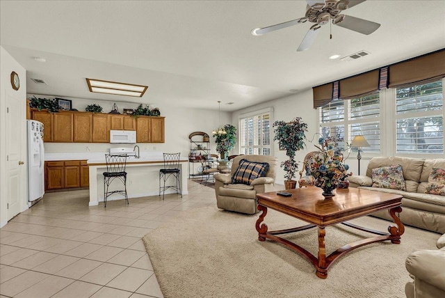 living area with a ceiling fan, visible vents, plenty of natural light, and light tile patterned floors