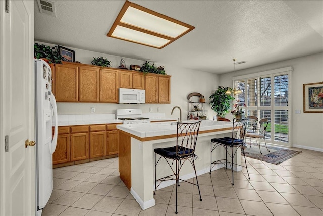 kitchen featuring light tile patterned flooring, white appliances, a breakfast bar, visible vents, and brown cabinets