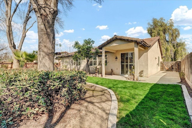 rear view of property with stucco siding, a lawn, a patio area, fence, and a tiled roof