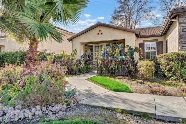 doorway to property featuring a tile roof, fence, and stucco siding