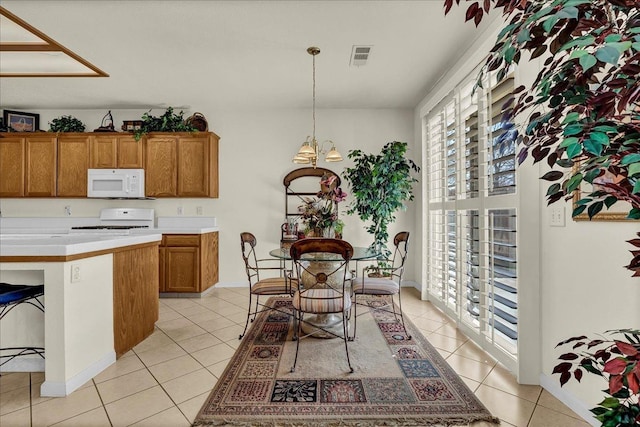 kitchen featuring light tile patterned floors, white microwave, range, brown cabinetry, and decorative light fixtures