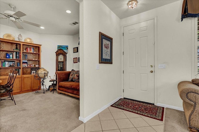 entryway with light tile patterned floors, light colored carpet, visible vents, a ceiling fan, and baseboards