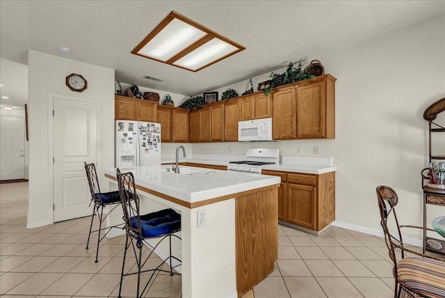 kitchen featuring light tile patterned floors, white appliances, a sink, a kitchen breakfast bar, and brown cabinets