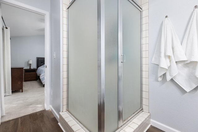 ensuite bathroom with connected bathroom, baseboards, wood finished floors, and a shower stall