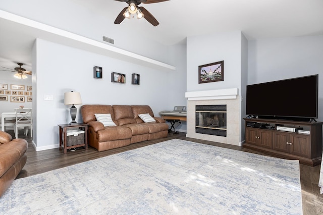 living room with visible vents, baseboards, a tiled fireplace, wood finished floors, and a ceiling fan