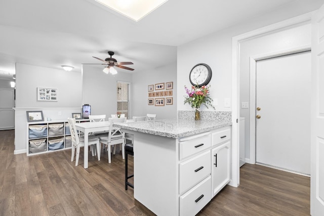 kitchen with a kitchen bar, light stone counters, dark wood-style floors, white cabinetry, and a ceiling fan