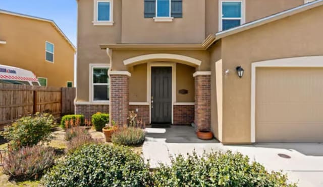 entrance to property featuring stucco siding, fence, and brick siding