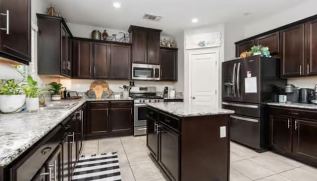kitchen with light tile patterned floors, a kitchen island, visible vents, light stone countertops, and appliances with stainless steel finishes