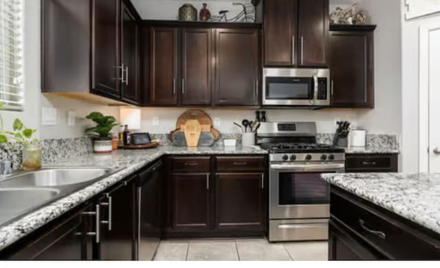 kitchen with light tile patterned flooring, light stone countertops, stainless steel appliances, and dark brown cabinets