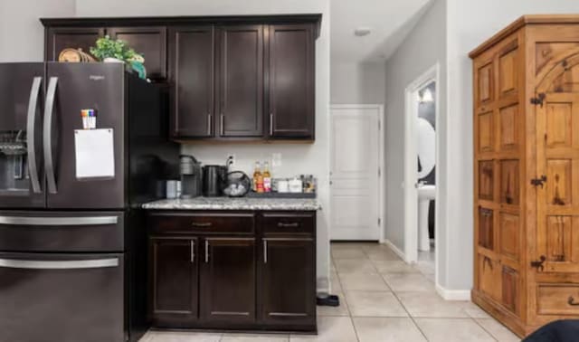 kitchen with dark brown cabinets, stainless steel fridge with ice dispenser, baseboards, and light tile patterned floors