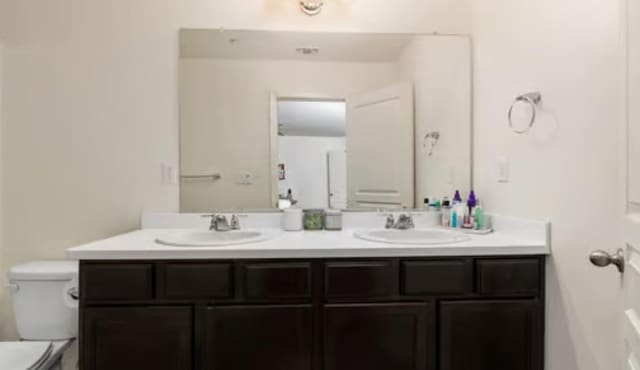 full bathroom with double vanity, a sink, and toilet