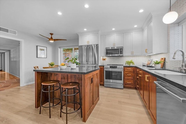 kitchen featuring stainless steel appliances, visible vents, light wood-style flooring, a sink, and a kitchen breakfast bar