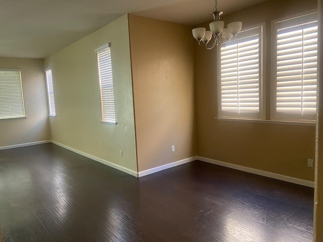 empty room featuring a chandelier, dark wood finished floors, and baseboards