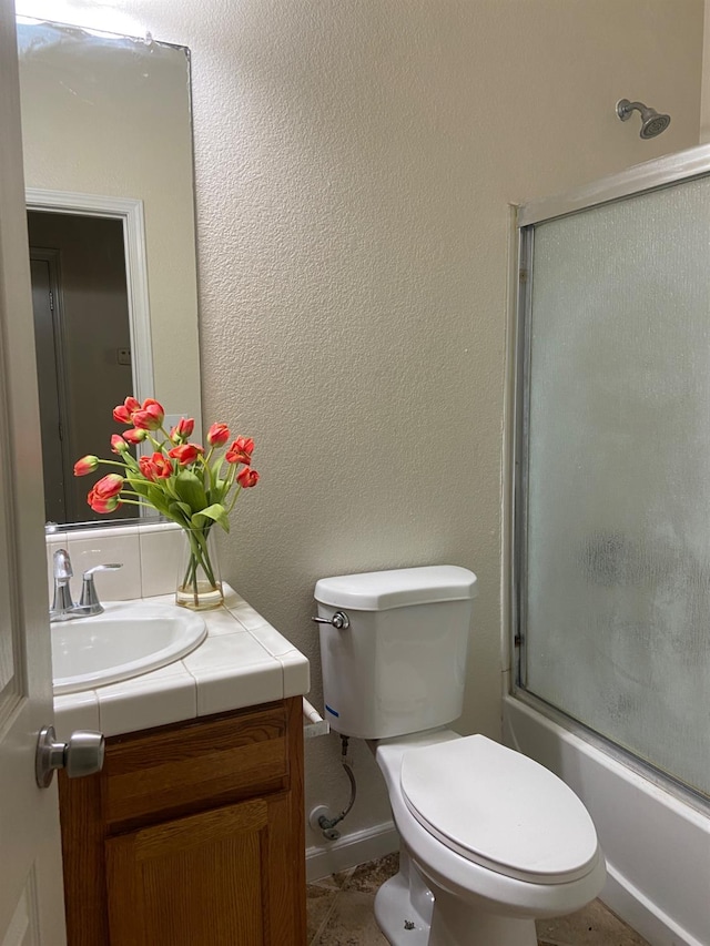 bathroom featuring a textured wall, shower / bath combination with glass door, vanity, and toilet