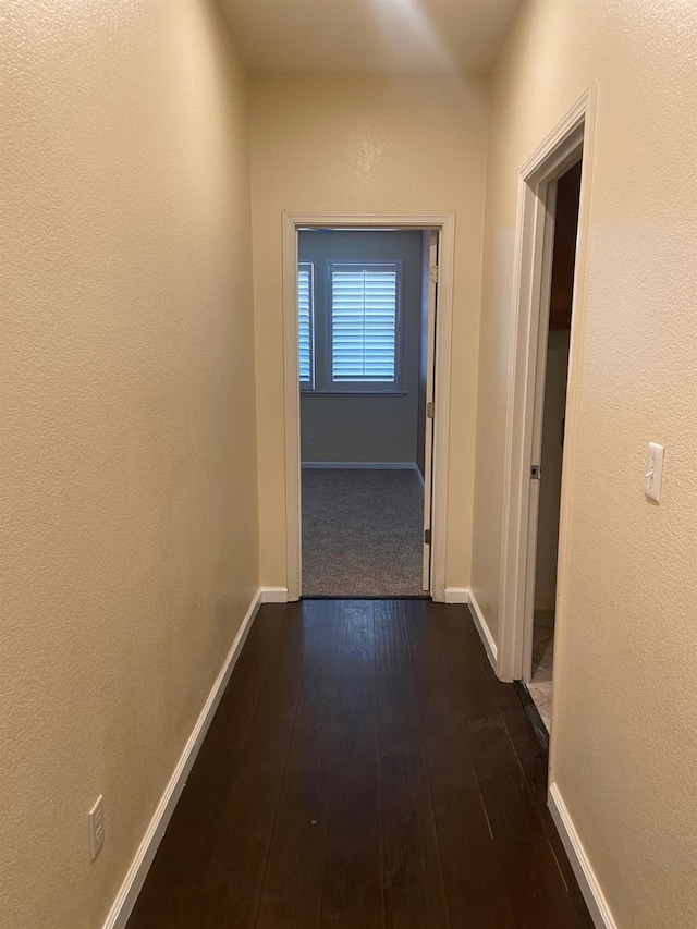 hallway with baseboards, dark wood-type flooring, and a textured wall