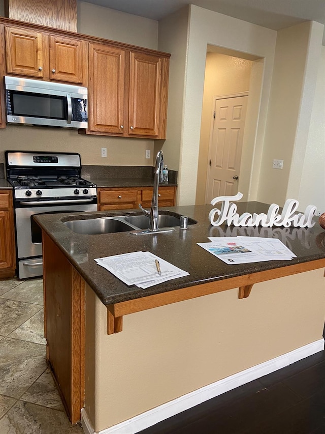 kitchen featuring appliances with stainless steel finishes, a sink, a center island with sink, and a kitchen breakfast bar