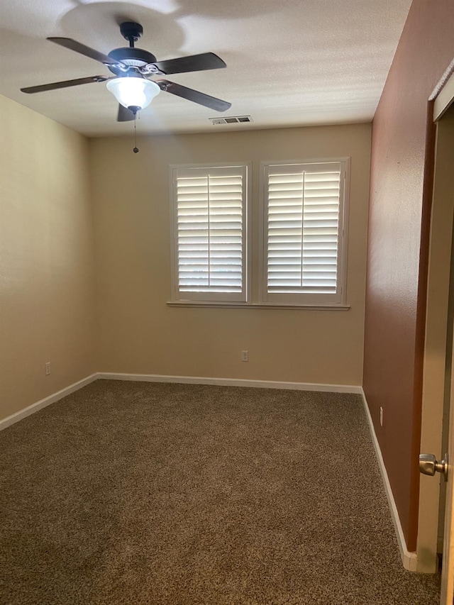 carpeted spare room featuring baseboards, visible vents, and ceiling fan