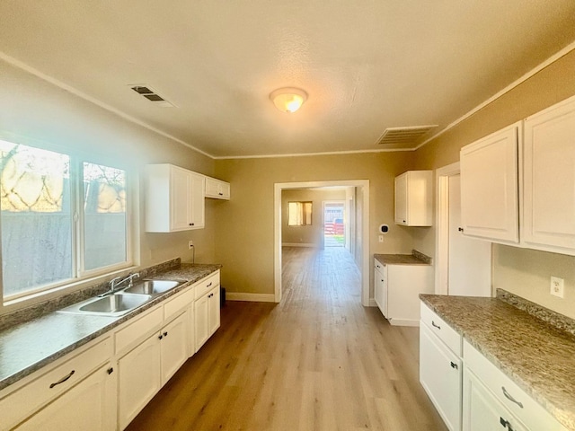 kitchen featuring a sink, visible vents, baseboards, white cabinetry, and light wood-type flooring