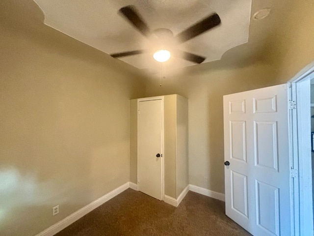 unfurnished bedroom featuring dark carpet, baseboards, and ceiling fan