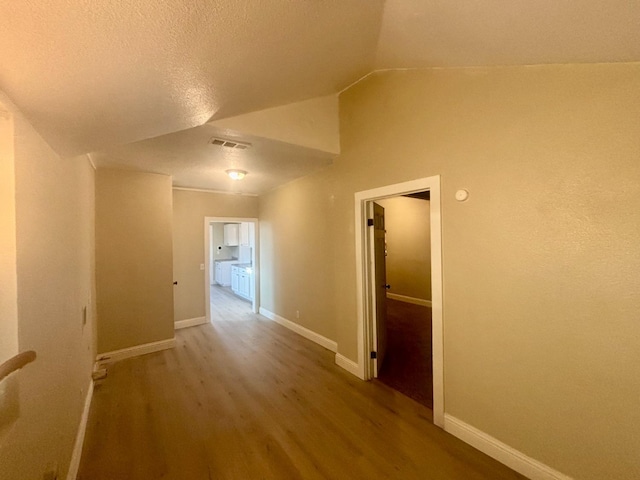 hallway with lofted ceiling, visible vents, a textured ceiling, wood finished floors, and baseboards