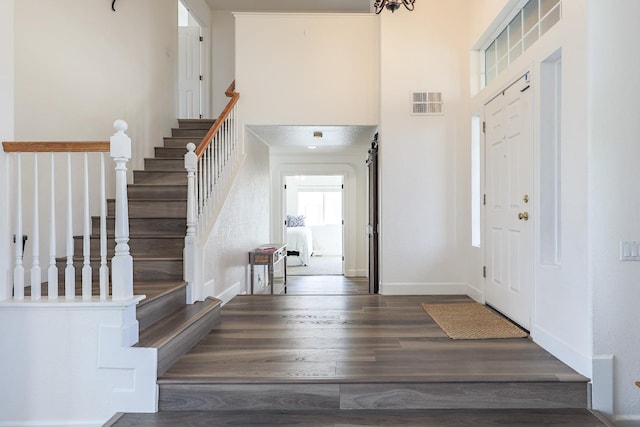 entryway with stairway, a high ceiling, visible vents, and dark wood finished floors