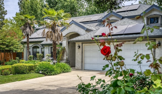 view of front of home featuring a garage, solar panels, fence, concrete driveway, and stucco siding