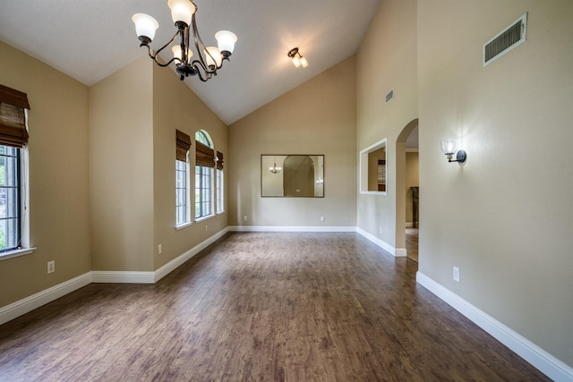 empty room with arched walkways, dark wood-style flooring, visible vents, a chandelier, and baseboards