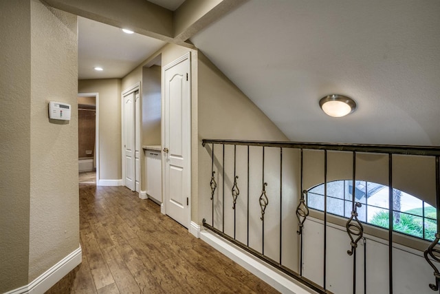 hallway with a textured wall, wood finished floors, and baseboards