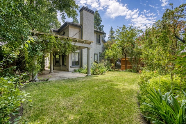 rear view of property featuring fence, a yard, stucco siding, a chimney, and a patio area