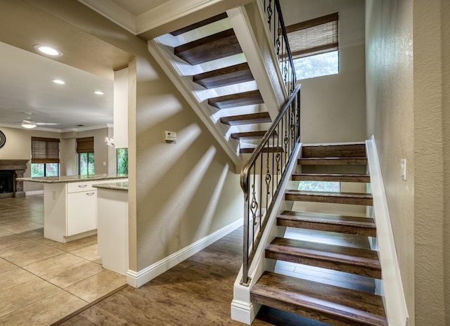 staircase featuring a healthy amount of sunlight, a fireplace, baseboards, and a ceiling fan